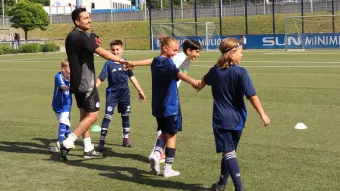 Eine Gruppe von Kindern kickt einen Fußball auf einem Spielfeld, voller Energie und Freude. Sie halten sich dabei an den Händen.