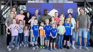 Gruppenfoto beim Familienfest von Schalke 04 mit Gerald Asamoah in der Mitte, umgeben von fröhlichen Kindern und Erwachsenen in Fantrikots.
