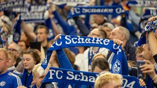 Fans im Stadion halten Schalke-Schals hoch.