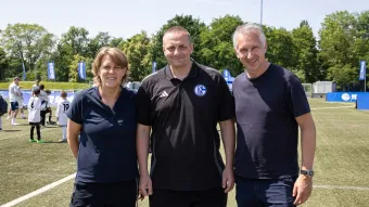 Christina Rühl-Hamers, Boris Liebing und Frank Baumann stehen auf dem Kunstrasen vor der Schalker Geschäftstelle.