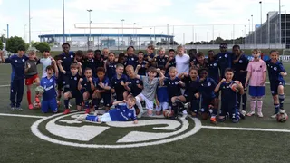 Eine große Gruppe von jubelnden Kindern stehen in zwei Reihen auf dem Rasen. Im Hintergrund ist die VELTINS-Arena sichtbar.