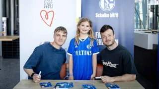 Ein junges Mädchen im Schalke-Trikot steht zwischen den Spielern Emil Højlund und Adrian Gantenbein bei einer Autogrammstunde beim Familienfest.