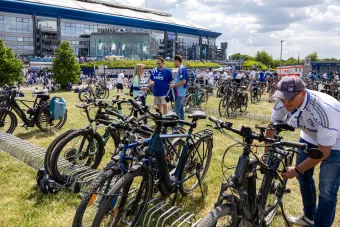Fans stellen ihre Fahrräder auf dem Rasen vor der Veltins-Arena in aufgestellten Fahrradständern ab.