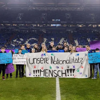 Ehrung der Städtischen Gesamtschule Suderwich aus Recklinghausen in der Veltins-Arena mit Schülern, die kleine und große Banner hochhalten vor der Tribüne.