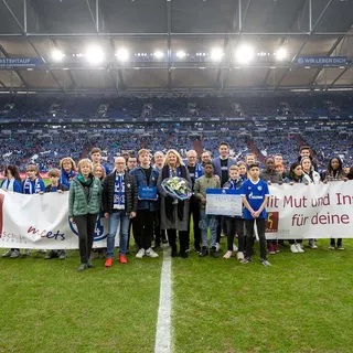 Ehrung der Rosa Parks Schulein der Veltins-Arena mit Schülern die ein großes Banner halten und einer Urkunde vor der Tribünen.