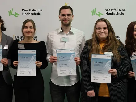 Fünf Personen stehen vor einer weißen Wand mit dem Aufdruck Westfälische Hochschule und Deutschland Stipendium, sie halten stolz eine Urkunde in der Hand.