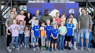 Gruppenfoto beim Familienfest von Schalke 04 mit Gerald Asamoah in der Mitte, umgeben von fröhlichen Kindern und Erwachsenen in Fantrikots.