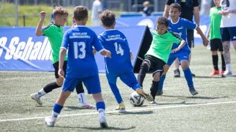 5 Kinder in blauen und grünen Trikots kämpfen auf dem Platz um den Ball.