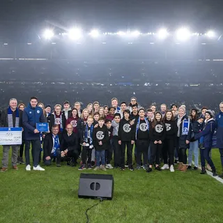 Ehrung des Internationalen Unternehmerverband RuhrStadt e.V auf dem Rasen in der Veltins-Arena mit Schülern, Urkunden vor vollen Tribünen.