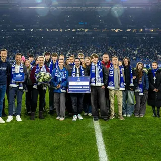 Ehrung auf dem Rasen in der Veltins-Arena mit Schülern, Blumen und Urkunde vor vollen Tribünen.