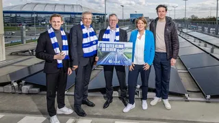 Das Bild zeigt die feierliche Einweihung der neuen Photovoltaikanlage des FC Schalke 04 auf dem Parkdeck am Stan-Libuda-Weg. Im Vordergrund stehen Vertreter des Vereins sowie der Projektpartner Emscher Lippe Energie GmbH (ELE) und Greenflash GmbH. Im Hintergrund sind die installierten Solarmodule zu sehen, die einen wichtigen Schritt in Richtung nachhaltiger Energieversorgung für das Vereinsgelände darstellen.