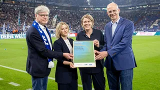 Vier Leute halten eine Urkunde im Stadion hoch.